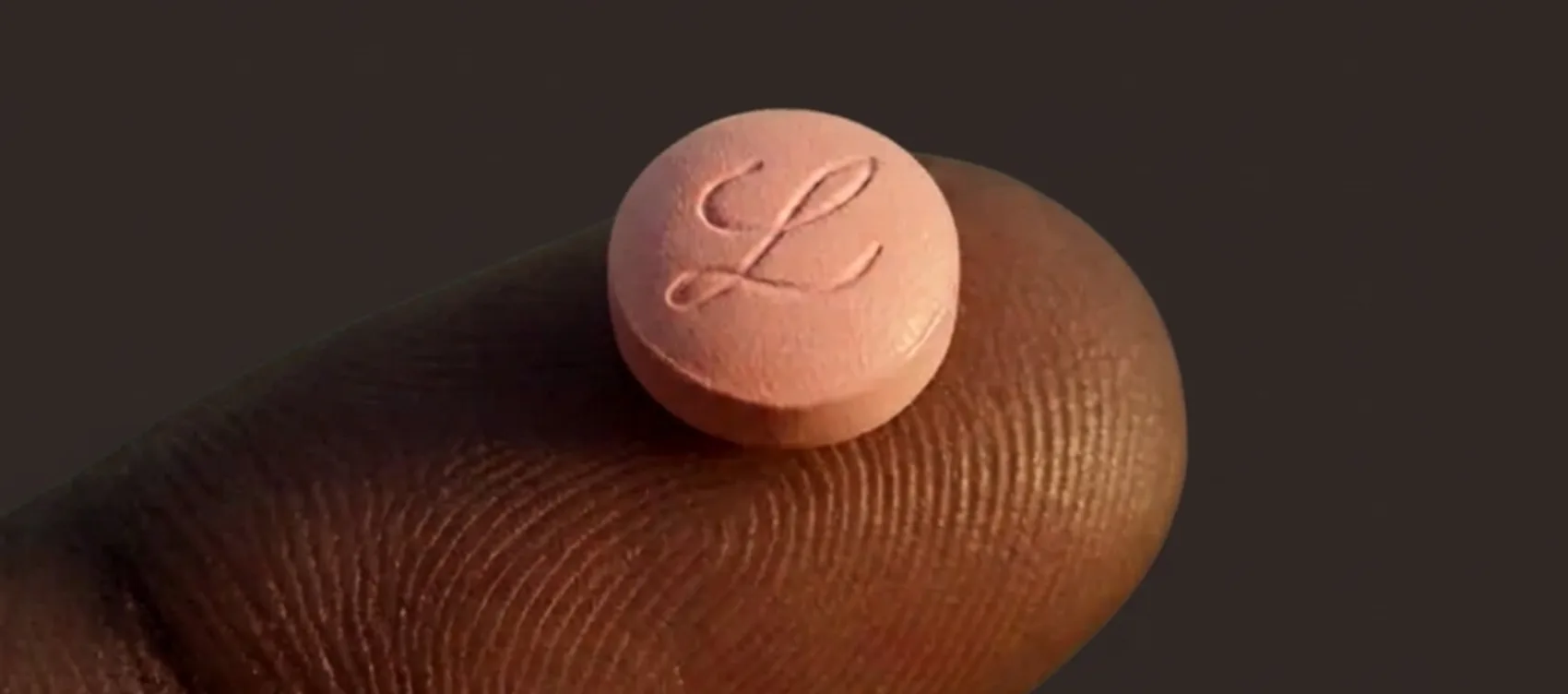 Illustration of a single pink orforglipron tablet resting on a fingertip